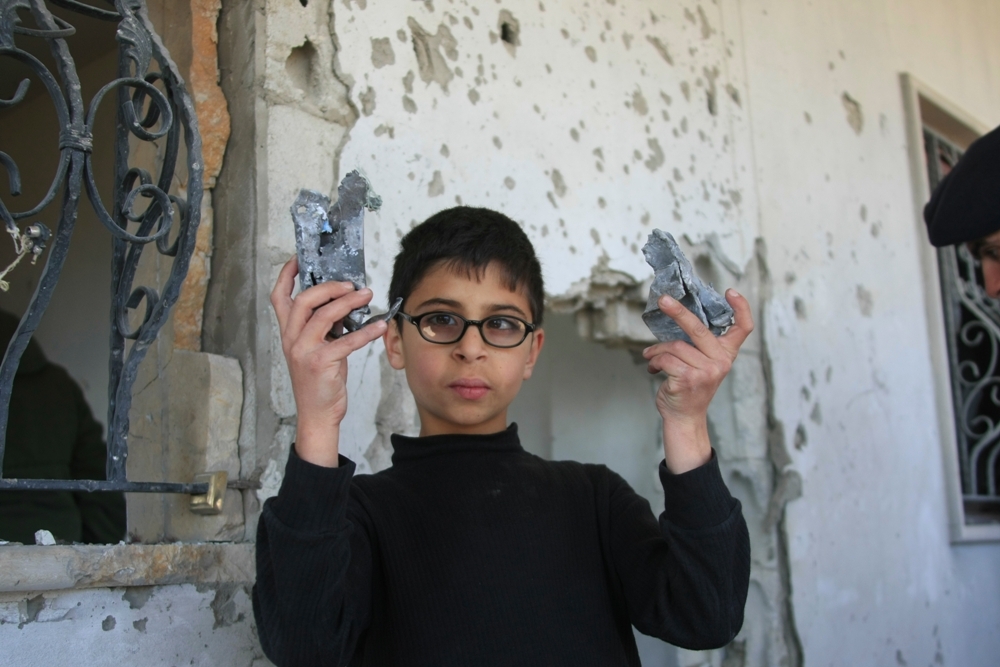 الطفل علي يحمل بيديه شظايا القذائف التي اصابت المنزل
